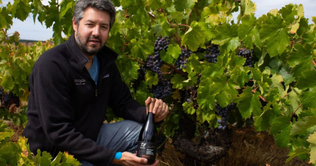 Fotografía de Rafael Urrejola en una viña tomando una botella de vino con sus manos