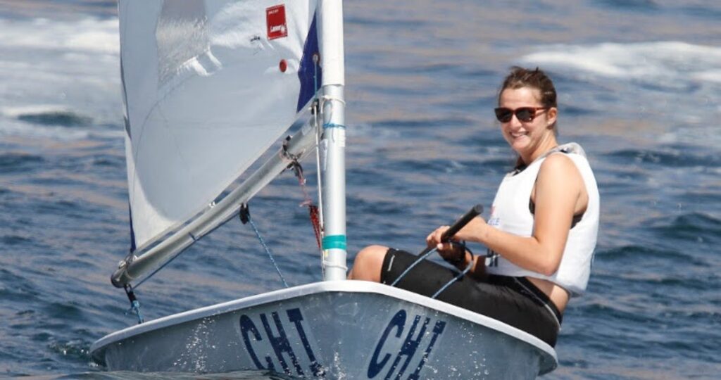 Fotografía de María José Poncell practicando velerismo sobre su velero en el mar, sonriendo y usando lentes de sol