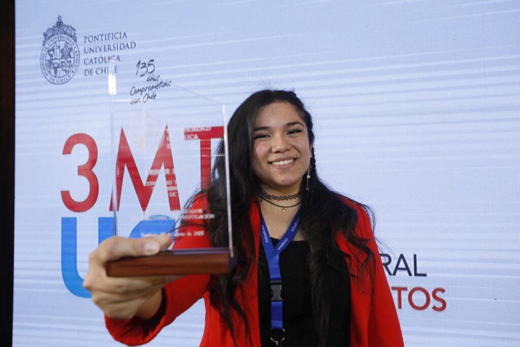 Fotografía de Macarena Droguett sonriendo y sosteniendo el premio al primer lugar en el concurso Tésis en 3 minutos edición 2023