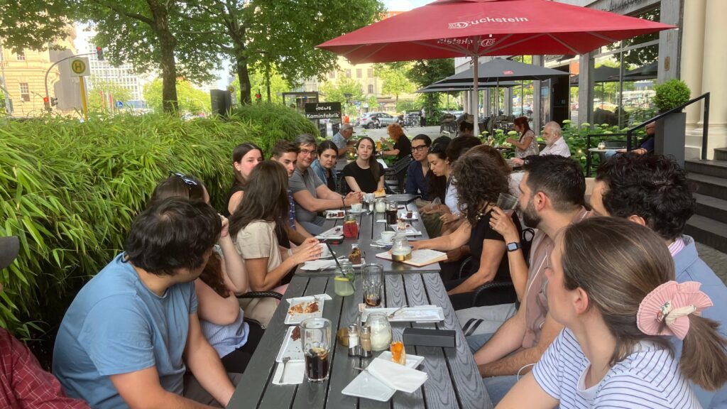 Fotografía de un grupo de más de 20 personas sentadas en una larga mesa converdando